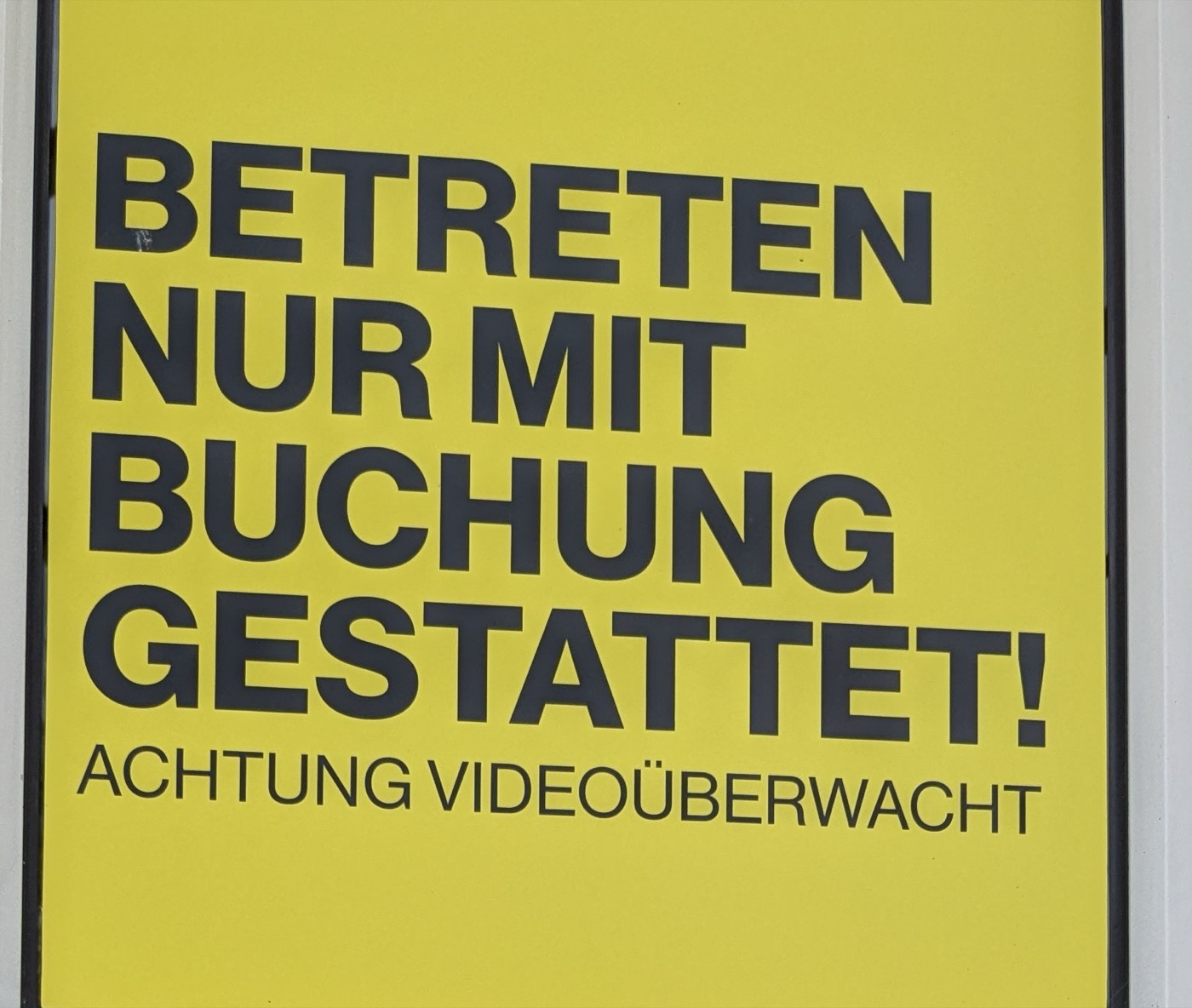 A yellow sign on a padel club door reading, in German, entry permitted only with a booking, warning: video surveillance